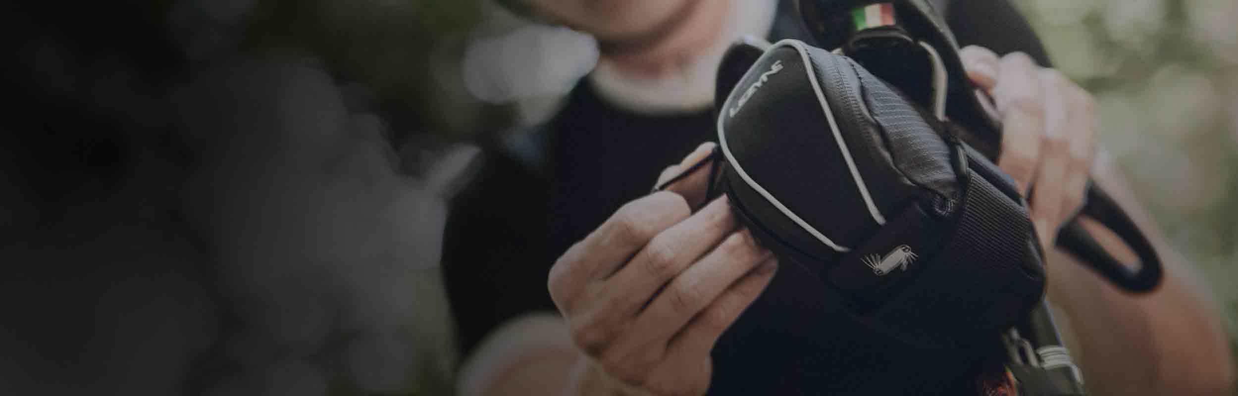 Someone unzipping a bag mounted to the bottom of a bicycle seat.