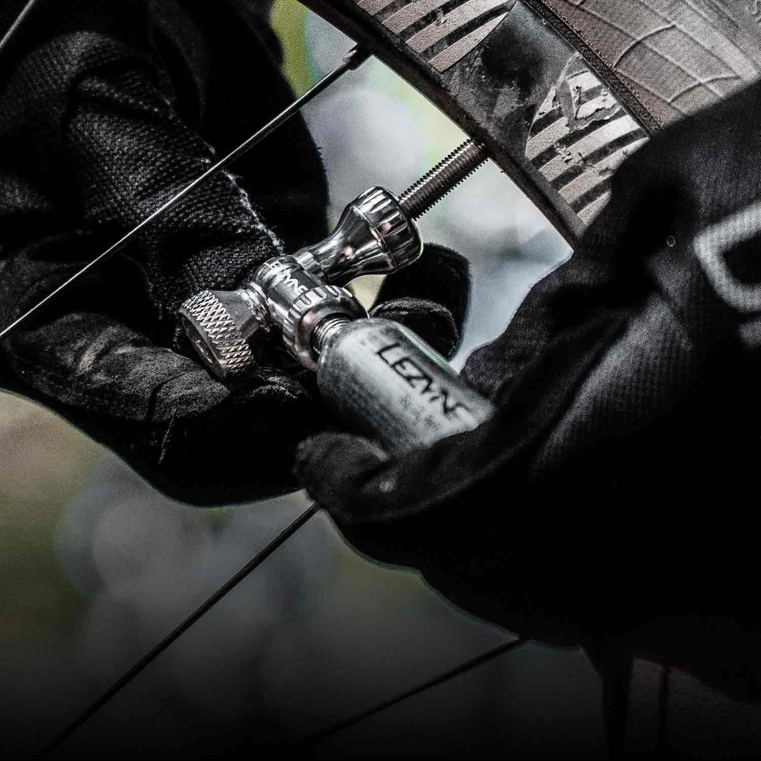 A closeup of gloved hands using a CO2 inflation canister to inflate a bicycle tire.