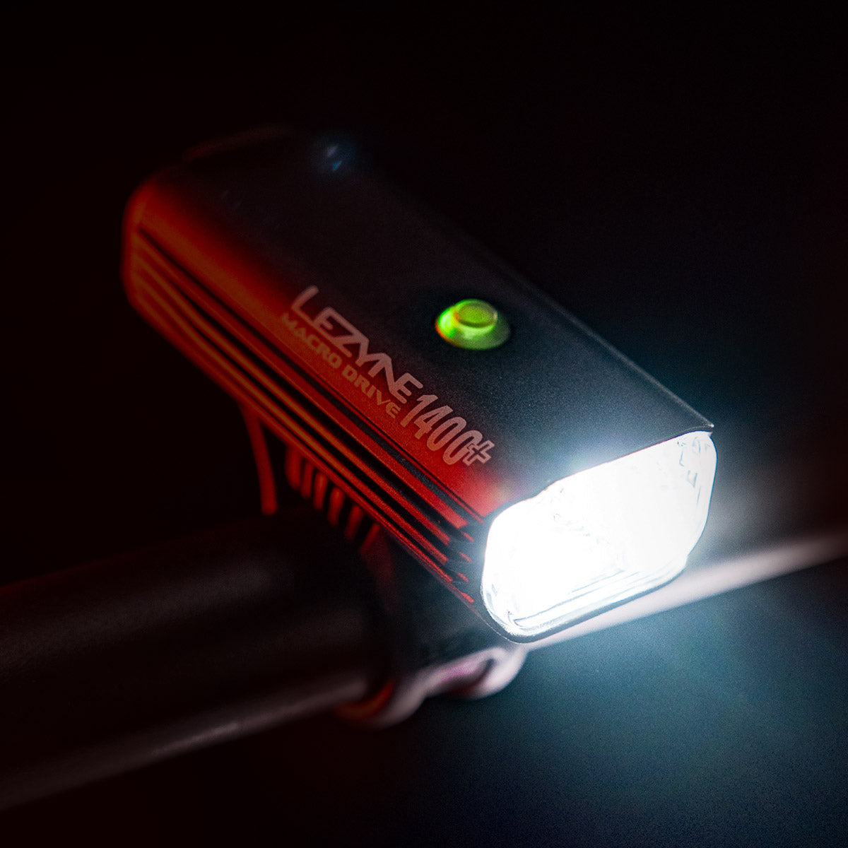 Front view of MACRO DRIVE 1400+ LED front bike light mounted on commuter bike, emitting super bright light with green power indicator.