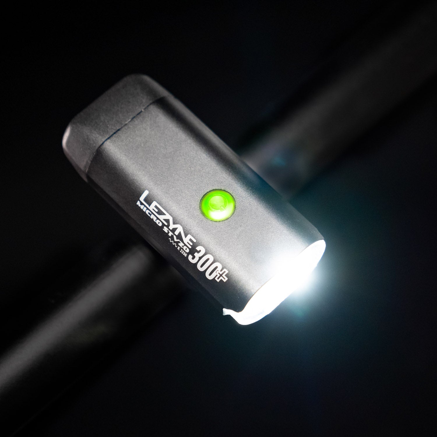 Bird's-eye view of the Lezyne Micro StVZO 300+ Bike Light, angled downwards to the right, with a green circular power button light on top and branding visible on the side, mounted on the handlebars.