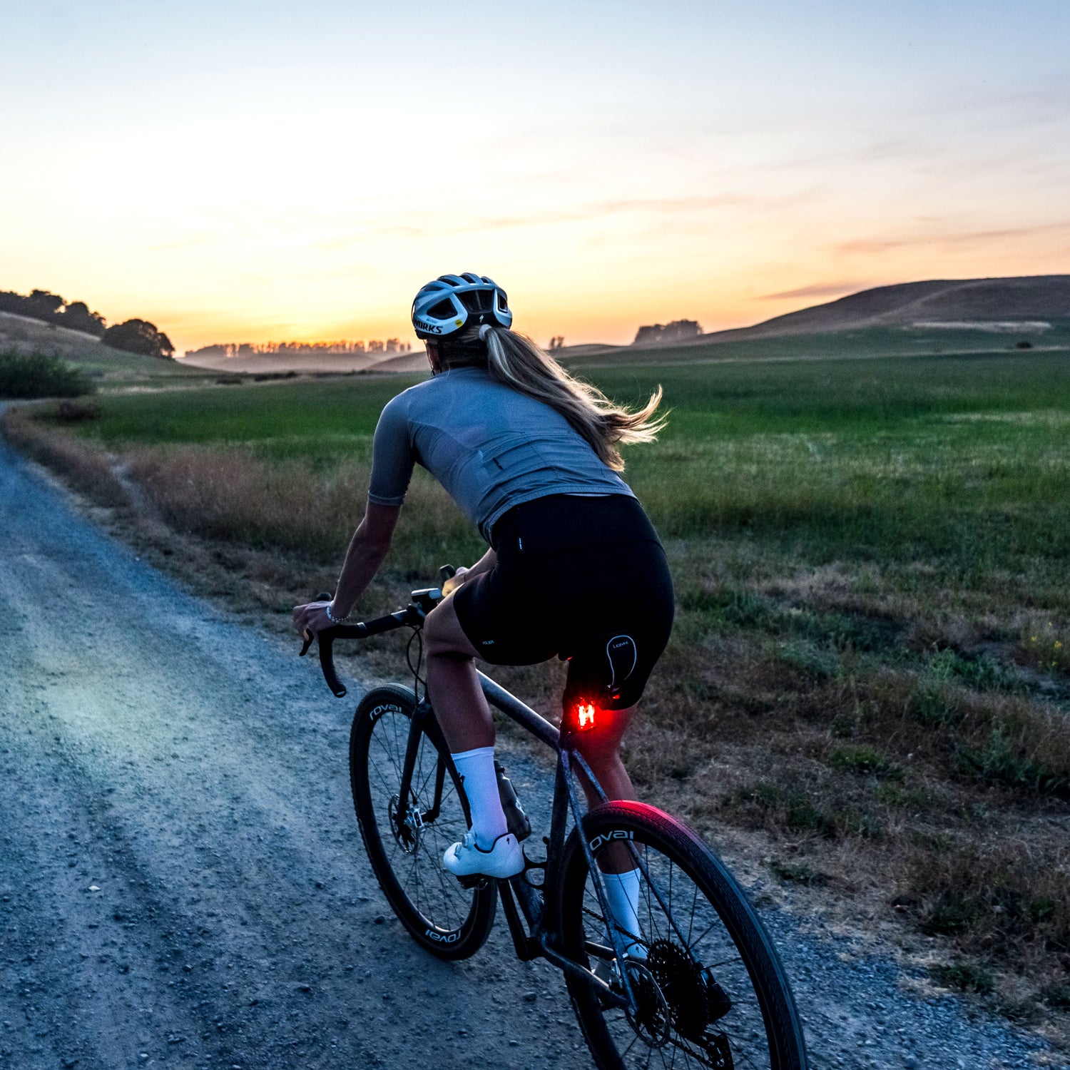 Lezyne Radar Drive LED rear bike light on cyclist riding at dusk; 300-lumen day flash active, road scene with low ambient light.