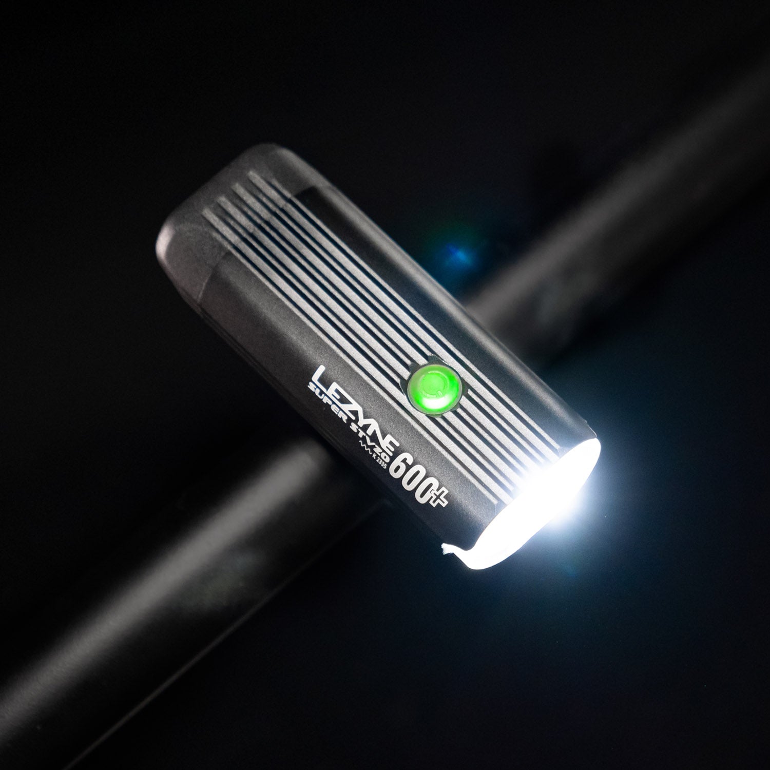 Bird's-eye view of the Lezyne Super StVZO 600+ Bike Light, angled towards the right, with a green circular power light on top, and emitting a bright white beam, mounted on handlebars.