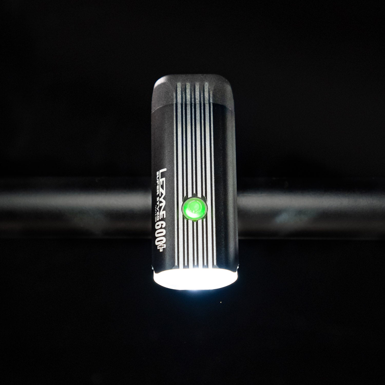 Bird's-eye view of the Lezyne Super StVZO 600+ LED headlight, with a green power button on top of housing, emitting a bright white beam, mounted on the handlebars.