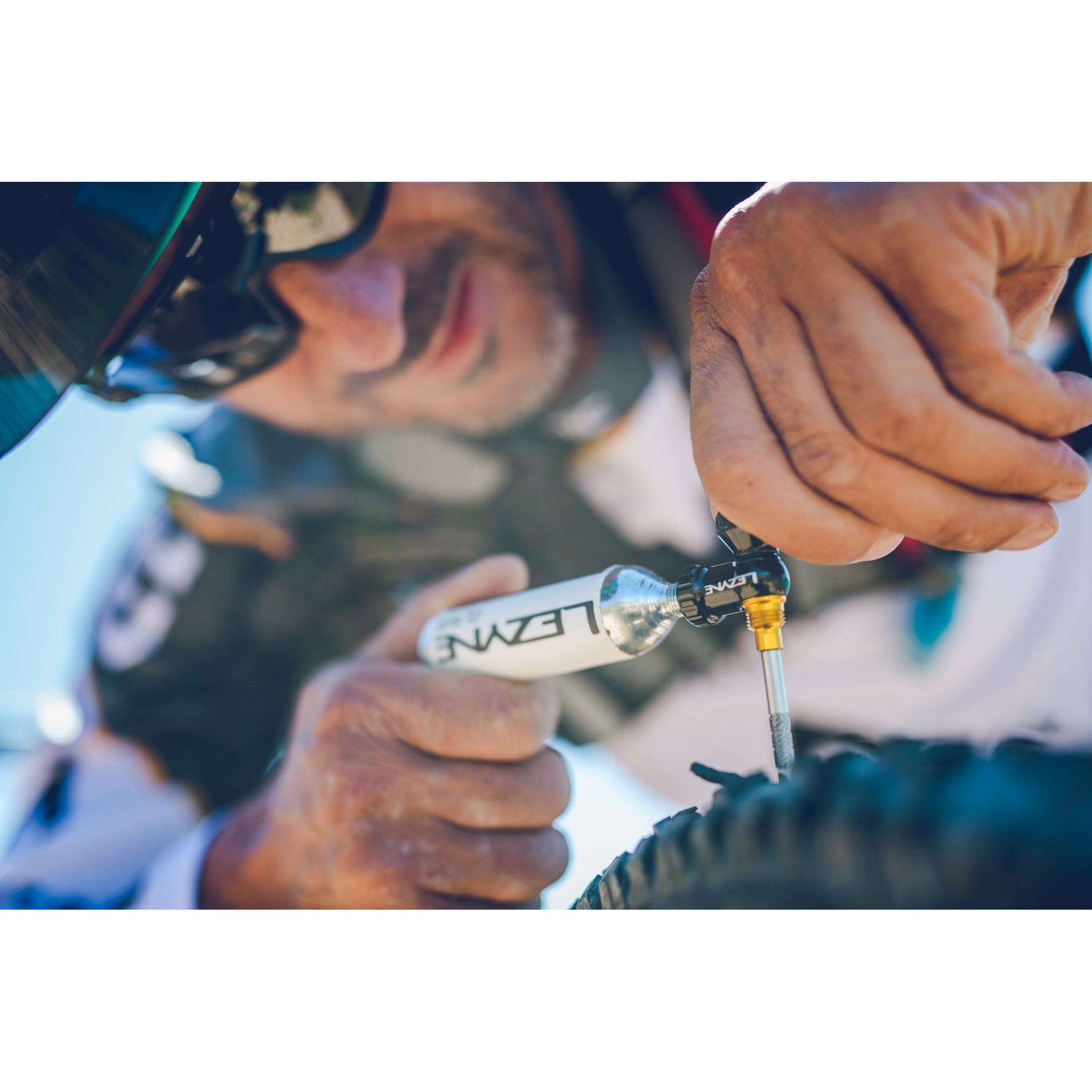 Mountain biker using the Lezyne CO2 Blaster to repair and inflate a tubeless tire mid-ride on the trail.