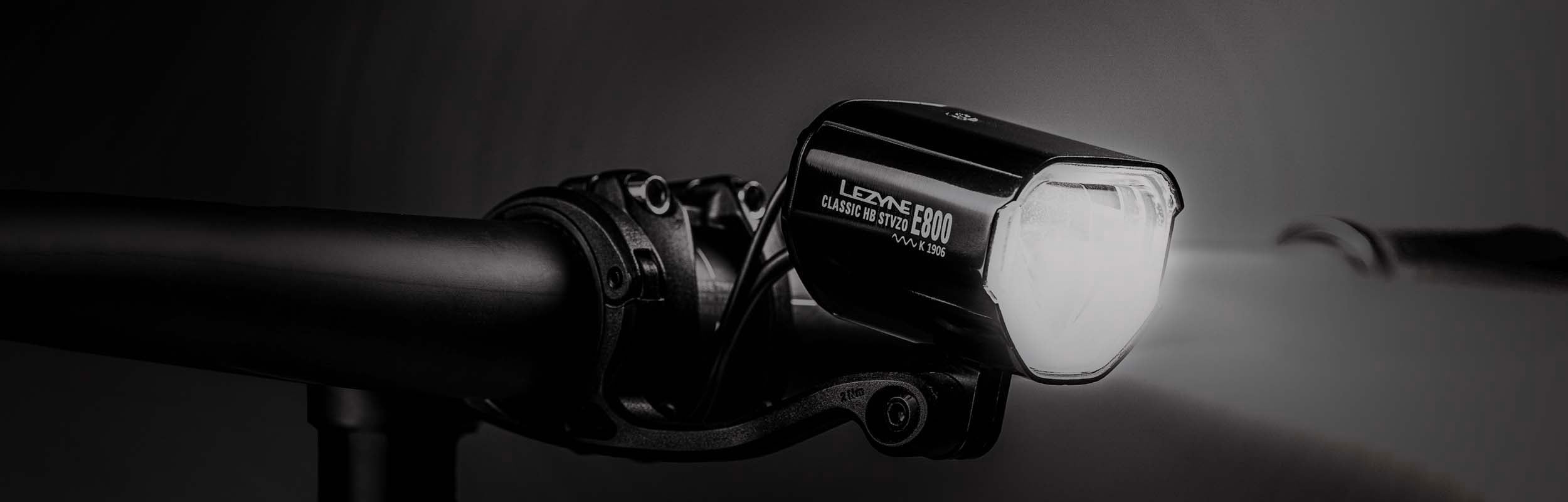 A bright light mounted on bicycle handlebars with Lezyne Classic HB STVZO E800 K 1906 printed on the side of the light.