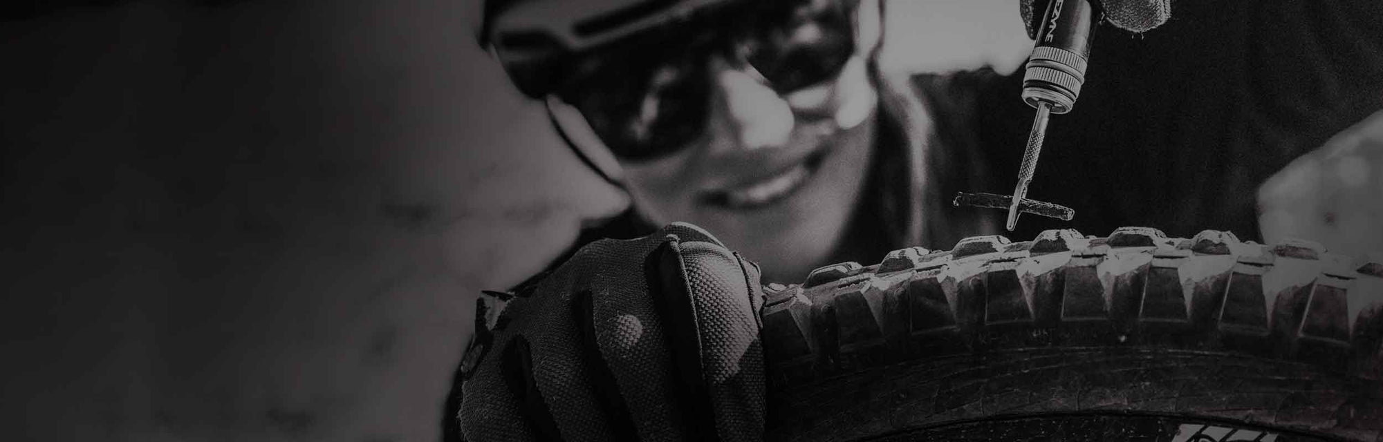 Someone holding a tool and a tire patch above a bicycle tire.