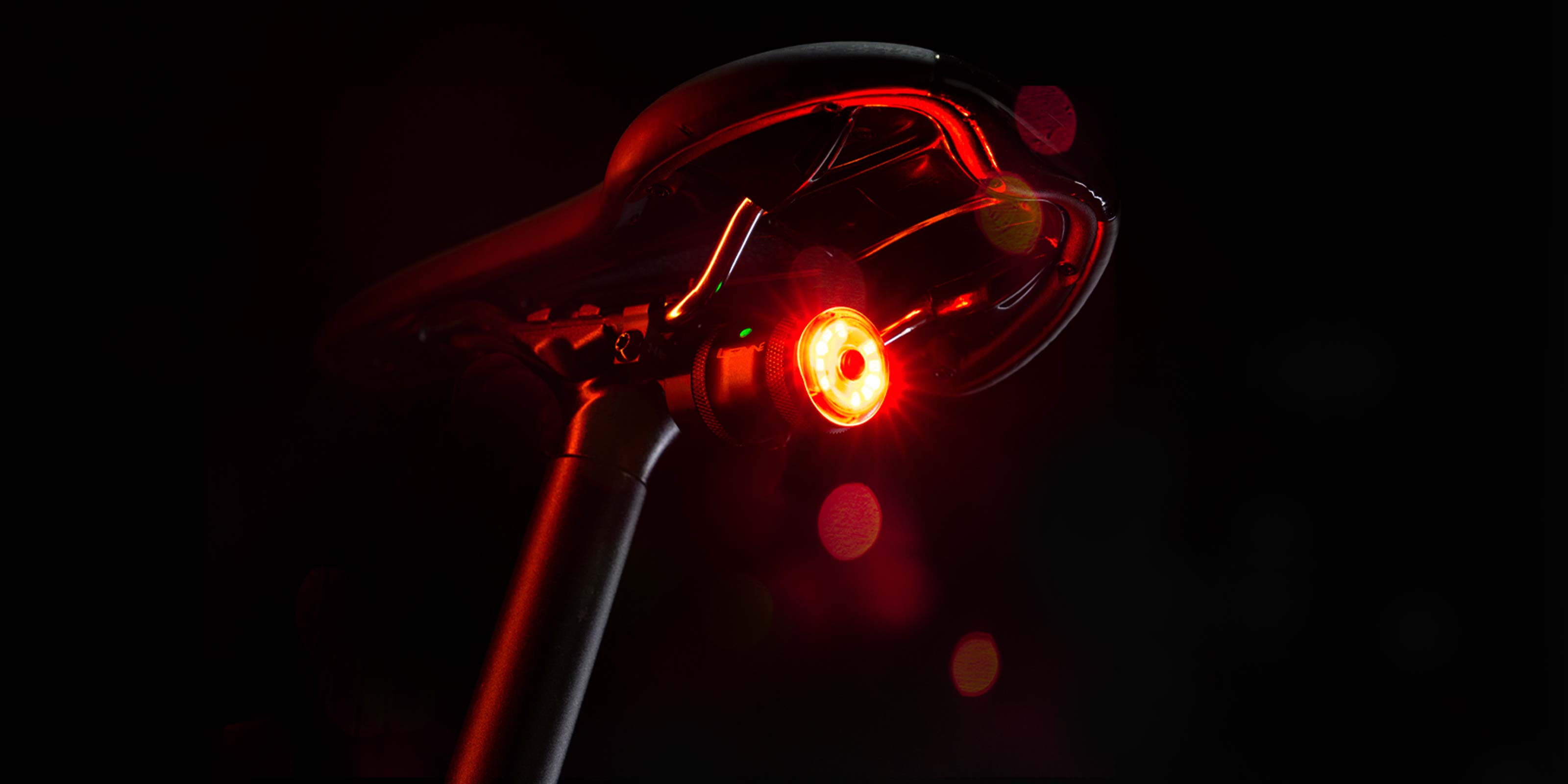 Close-up of the Lezyne Saddle AI Alert 250 bright red glowing LED rear light mounted on the black seat post of a road bike