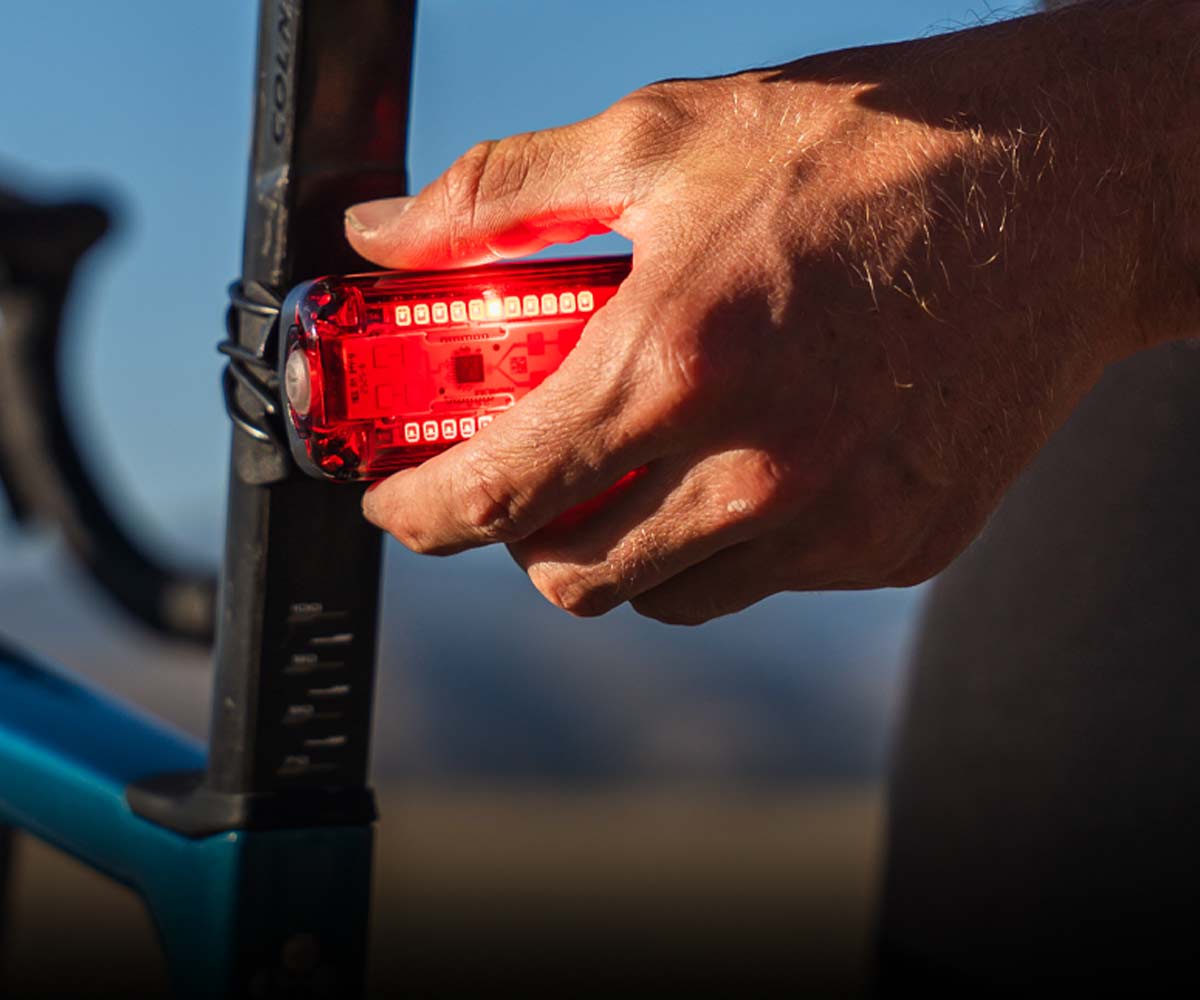 A close-up of a cyclist's hand holding a red illuminated Radar Pro 300 LED bicycle light.