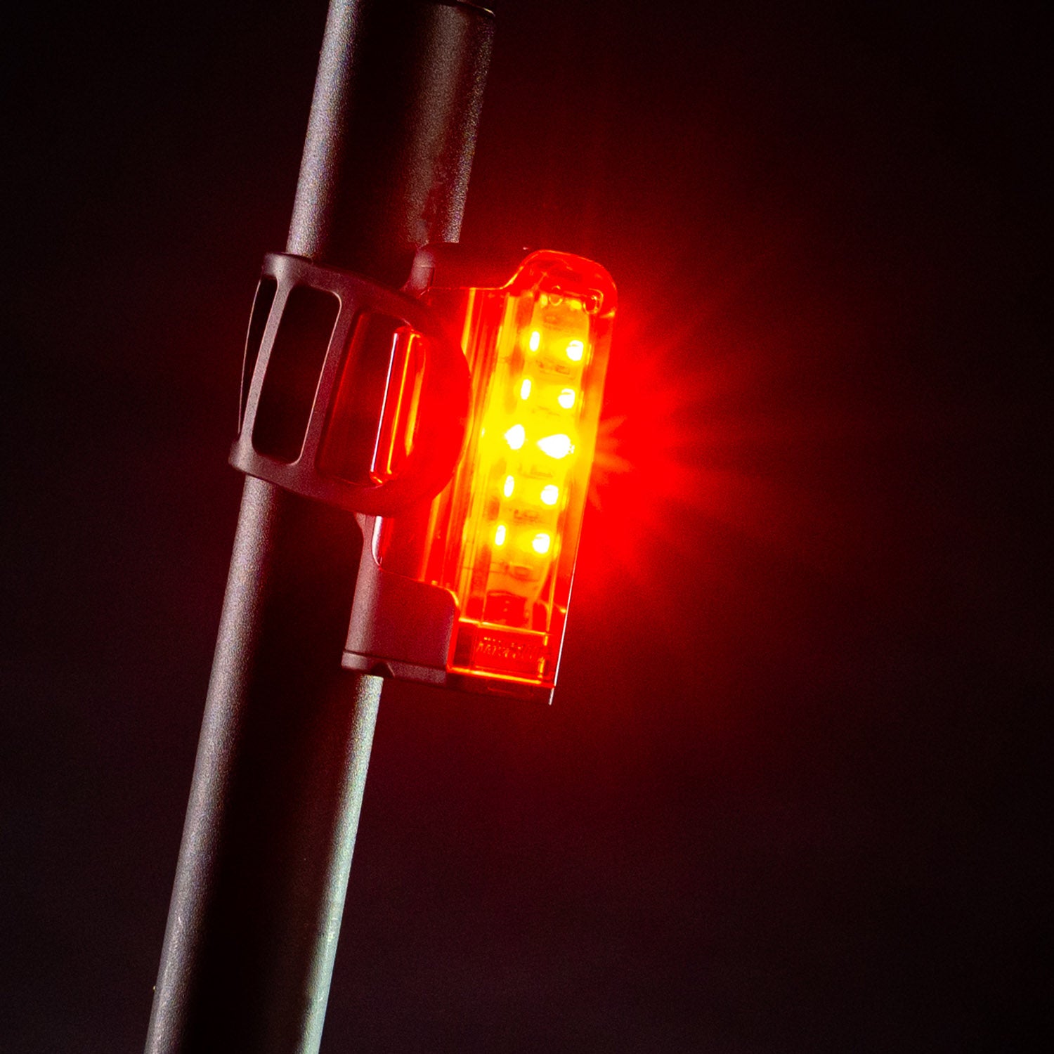 Side view of the Lezyne Strip+ StVZO LED Rear tail light, emitting a bright red light, mounted on the bike seat post.